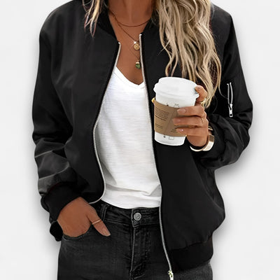 Person wearing a black jacket, white shirt, and dark jeans holding a coffee cup.